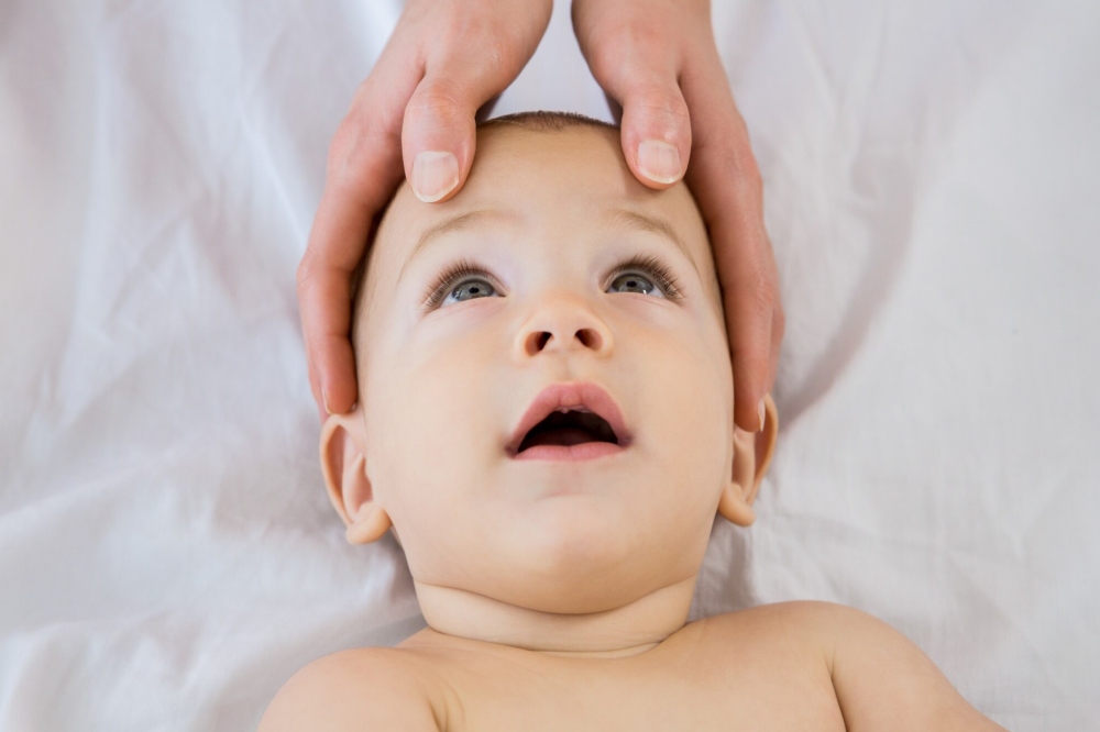 manos del fisio tocando la cabeza de un bebe